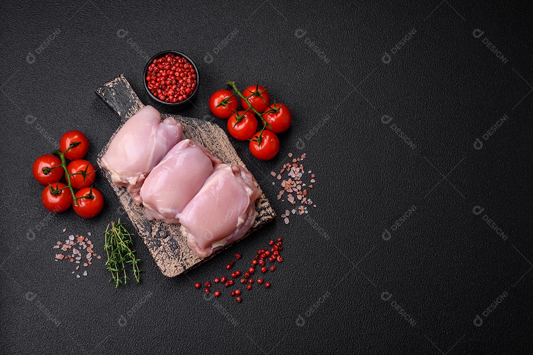 Filetes de coxa de frango cru fresco com sal, especiarias e ervas sobre um fundo escuro de concreto