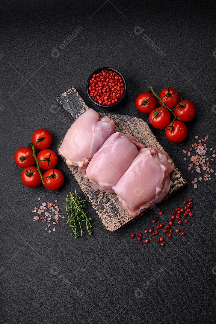 Filetes de coxa de frango cru fresco com sal, especiarias e ervas sobre um fundo escuro de concreto