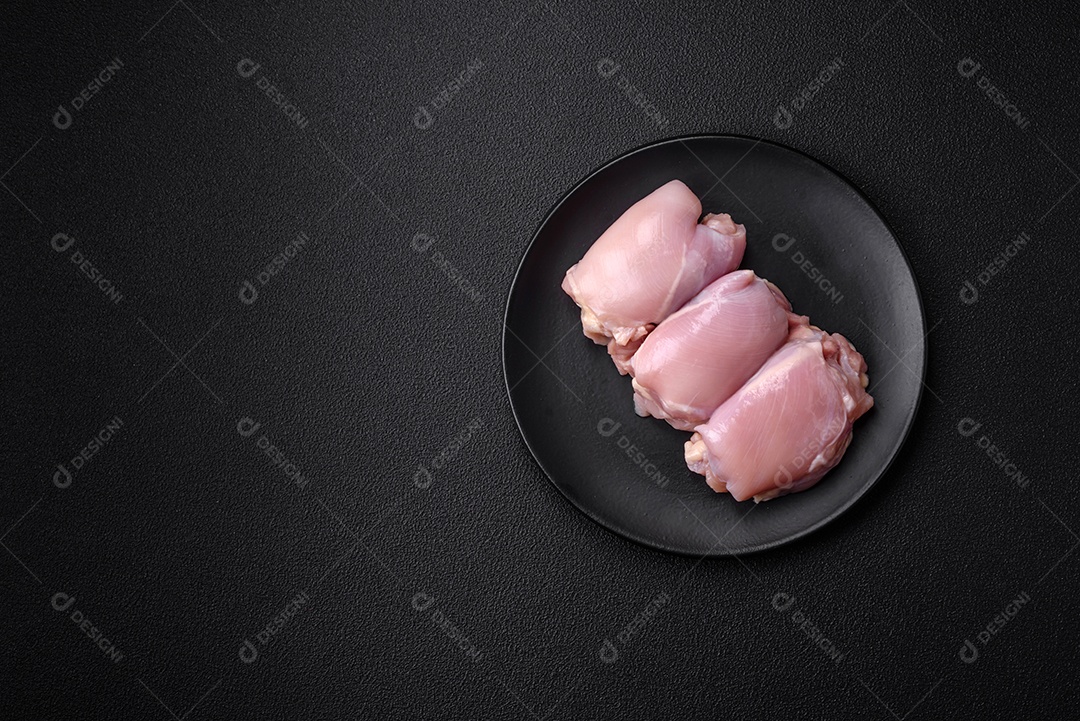 Filetes de coxa de frango cru fresco com sal, especiarias e ervas sobre um fundo escuro de concreto