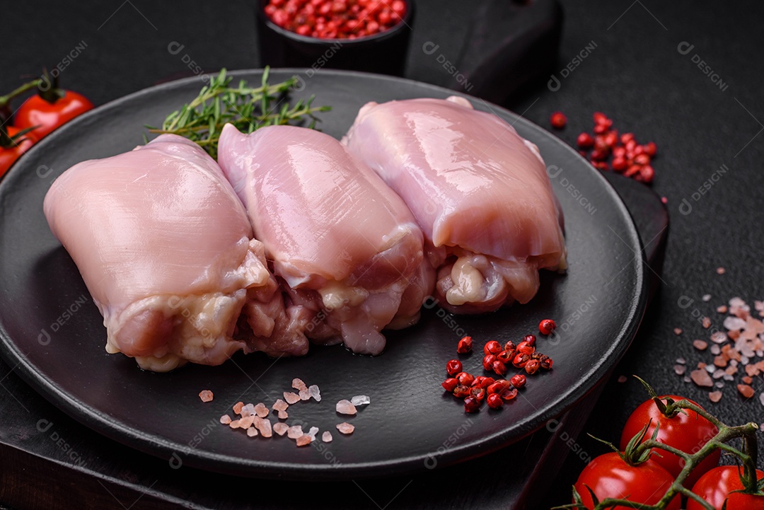 Filetes de coxa de frango cru fresco com sal, especiarias e ervas sobre um fundo escuro de concreto