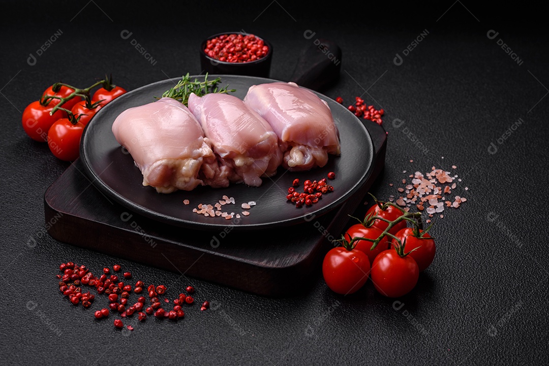 Filetes de coxa de frango cru fresco com sal, especiarias e ervas sobre um fundo escuro de concreto