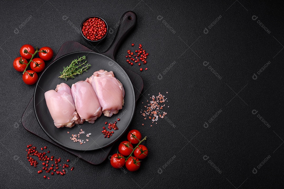 Filetes de coxa de frango cru fresco com sal, especiarias e ervas sobre um fundo escuro de concreto