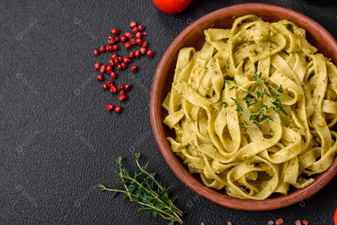 Deliciosa massa fresca com molho pesto, sal, especiarias e ervas num prato cerâmico sobre um fundo de concreto texturizado