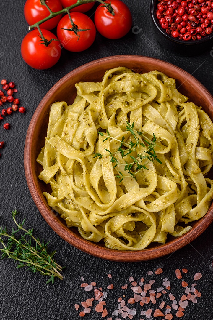 Deliciosa massa fresca com molho pesto, sal, especiarias e ervas num prato cerâmico sobre um fundo de concreto texturizado