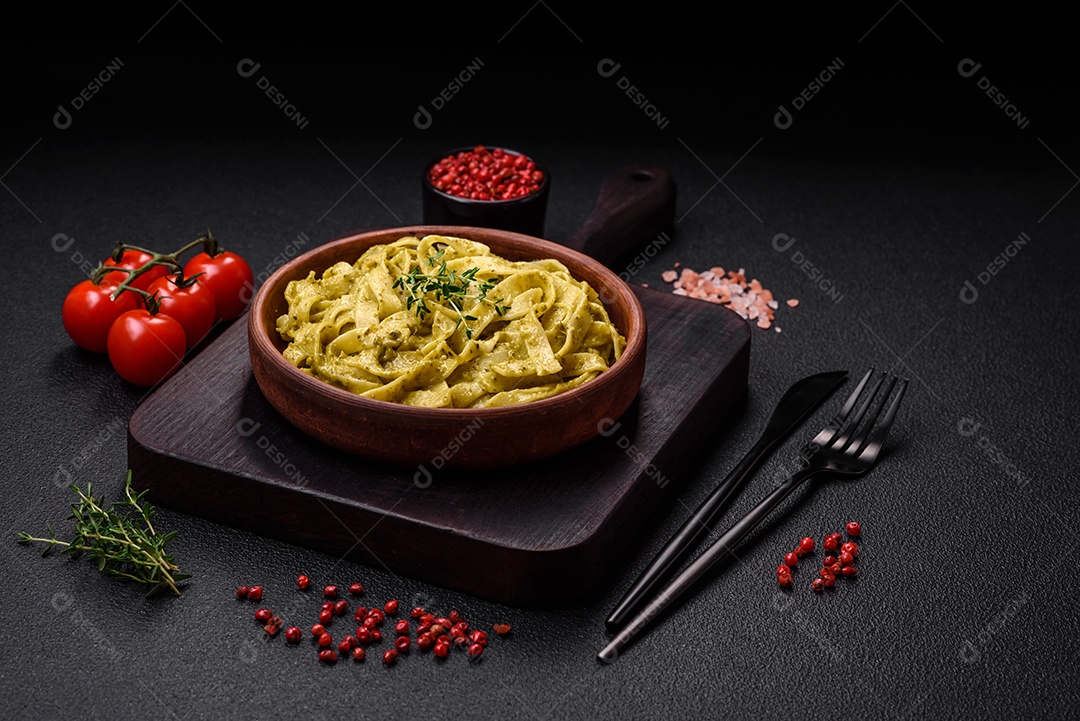 Deliciosa massa fresca com molho pesto, sal, especiarias e ervas num prato cerâmico sobre um fundo de concreto texturizado