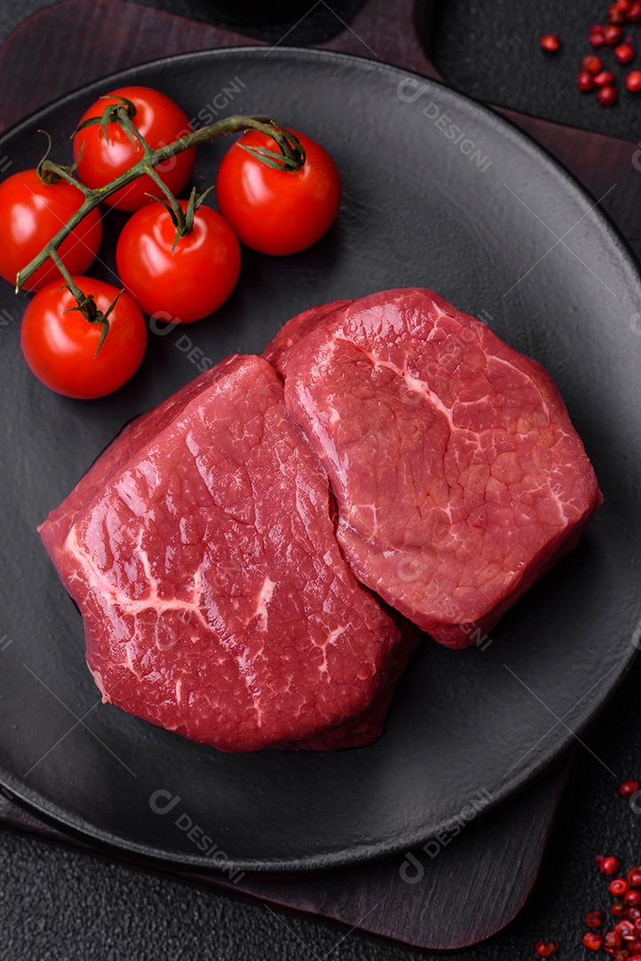 Bife de filé mignon cru com sal, especiarias e ervas em um fundo escuro de concreto