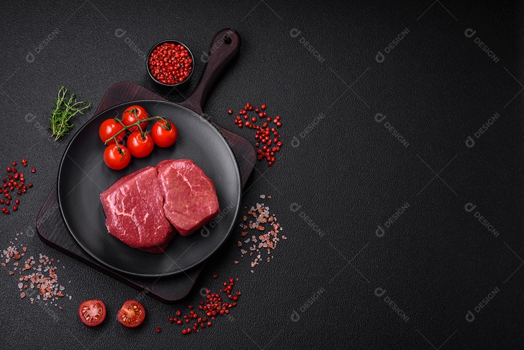 Bife de filé mignon cru com sal, especiarias e ervas em um fundo escuro de concreto