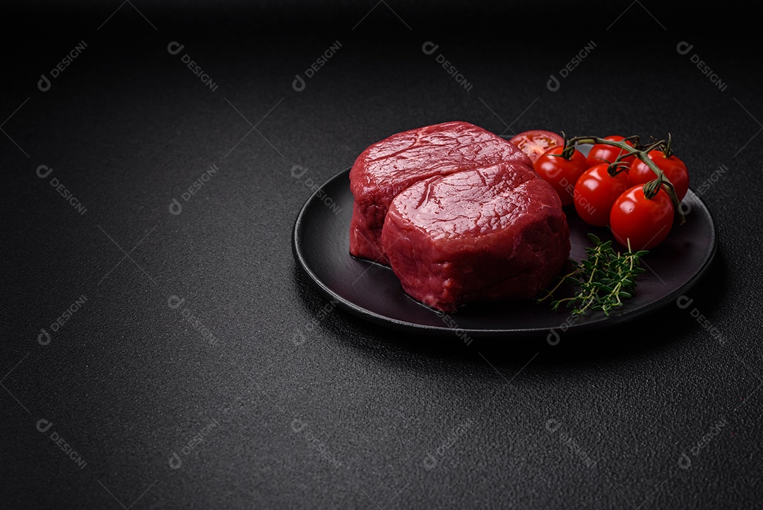 Bife de filé mignon cru com sal, especiarias e ervas em um fundo escuro de concreto