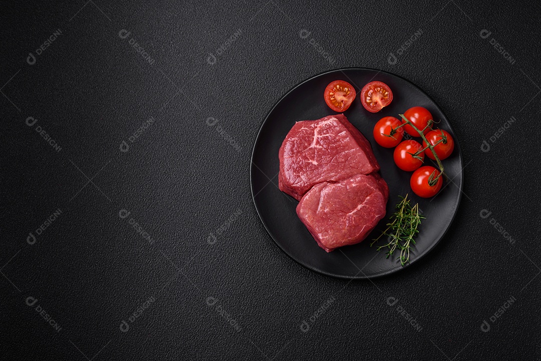 Bife de filé mignon cru com sal, especiarias e ervas em um fundo escuro de concreto