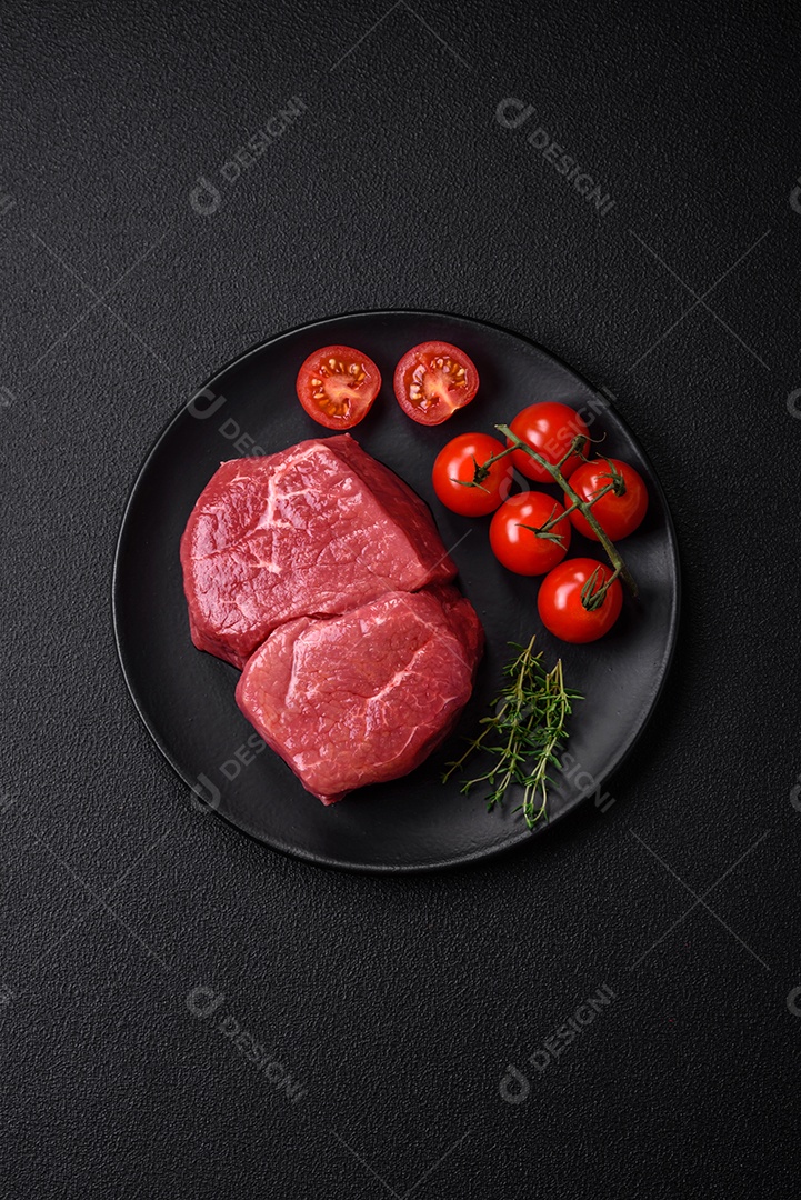 Bife de filé mignon cru com sal, especiarias e ervas em um fundo escuro de concreto