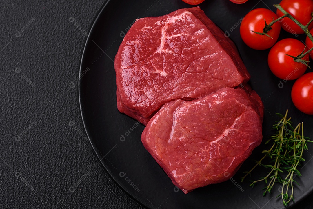 Bife de filé mignon cru com sal, especiarias e ervas em um fundo escuro de concreto