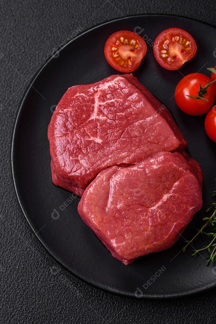 Bife de filé mignon cru com sal, especiarias e ervas em um fundo escuro de concreto