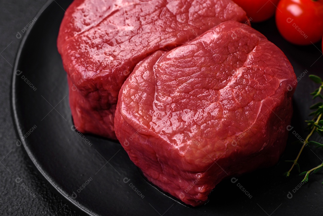 Bife de filé mignon cru com sal, especiarias e ervas em um fundo escuro de concreto