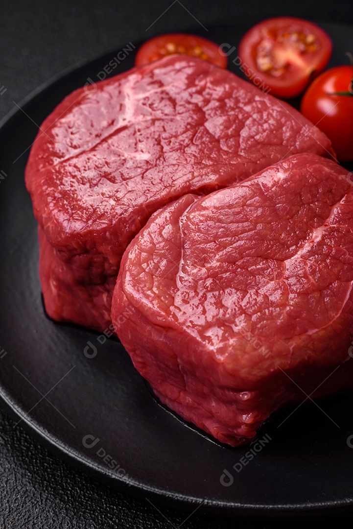 Bife de filé mignon cru com sal, especiarias e ervas em um fundo escuro de concreto