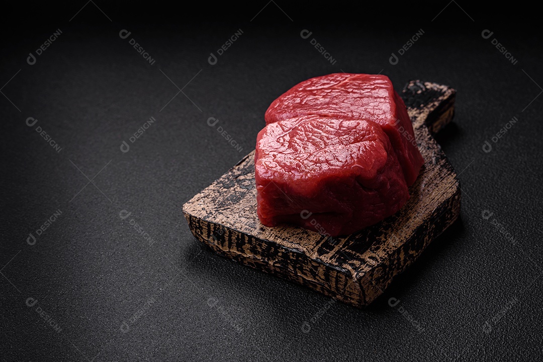 Bife de filé mignon cru com sal, especiarias e ervas em um fundo escuro de concreto