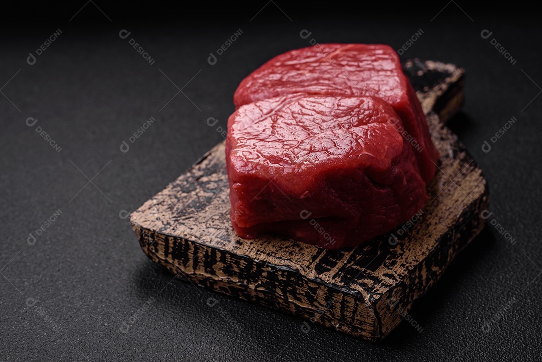 Bife de filé mignon cru com sal, especiarias e ervas em um fundo escuro de concreto