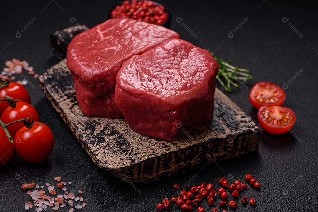 Bife de filé mignon cru com sal, especiarias e ervas em um fundo escuro de concreto