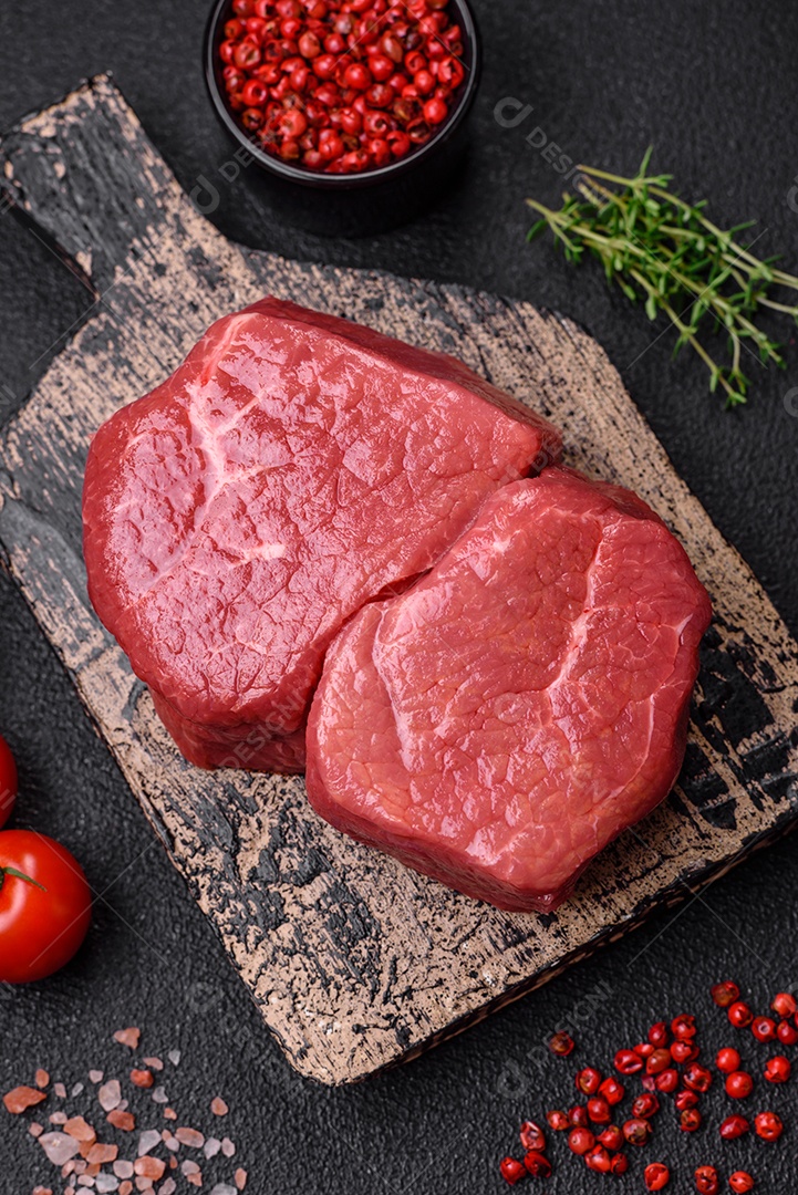 Bife de filé mignon cru com sal, especiarias e ervas em um fundo escuro de concreto