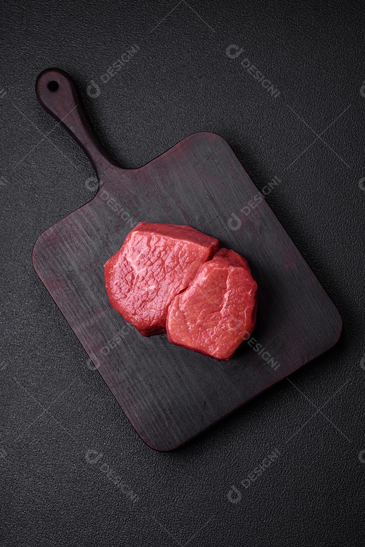 Bife de filé mignon cru com sal, especiarias e ervas em um fundo escuro de concreto