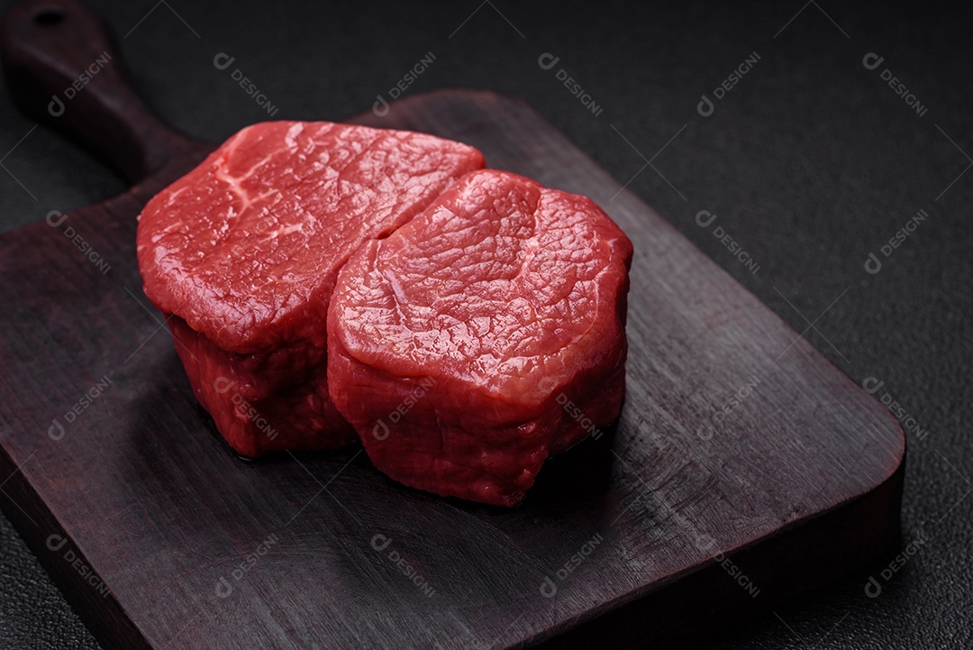 Bife de filé mignon cru com sal, especiarias e ervas em um fundo escuro de concreto