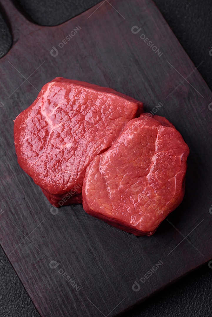 Bife de filé mignon cru com sal, especiarias e ervas em um fundo escuro de concreto