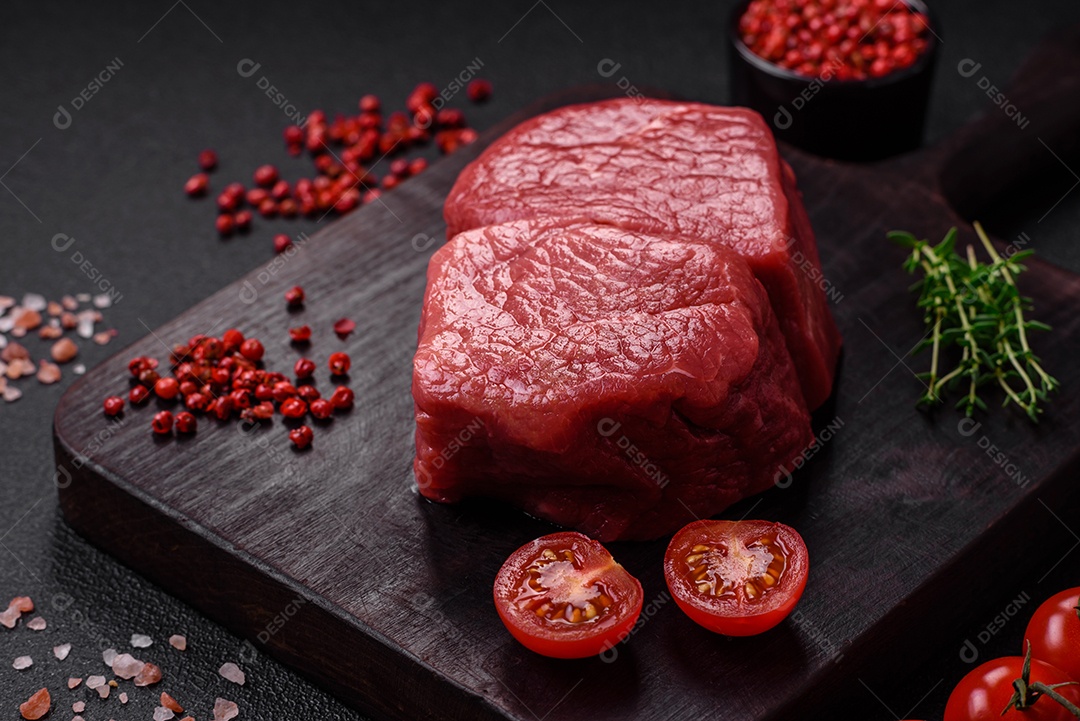 Bife de filé mignon cru com sal, especiarias e ervas em um fundo escuro de concreto