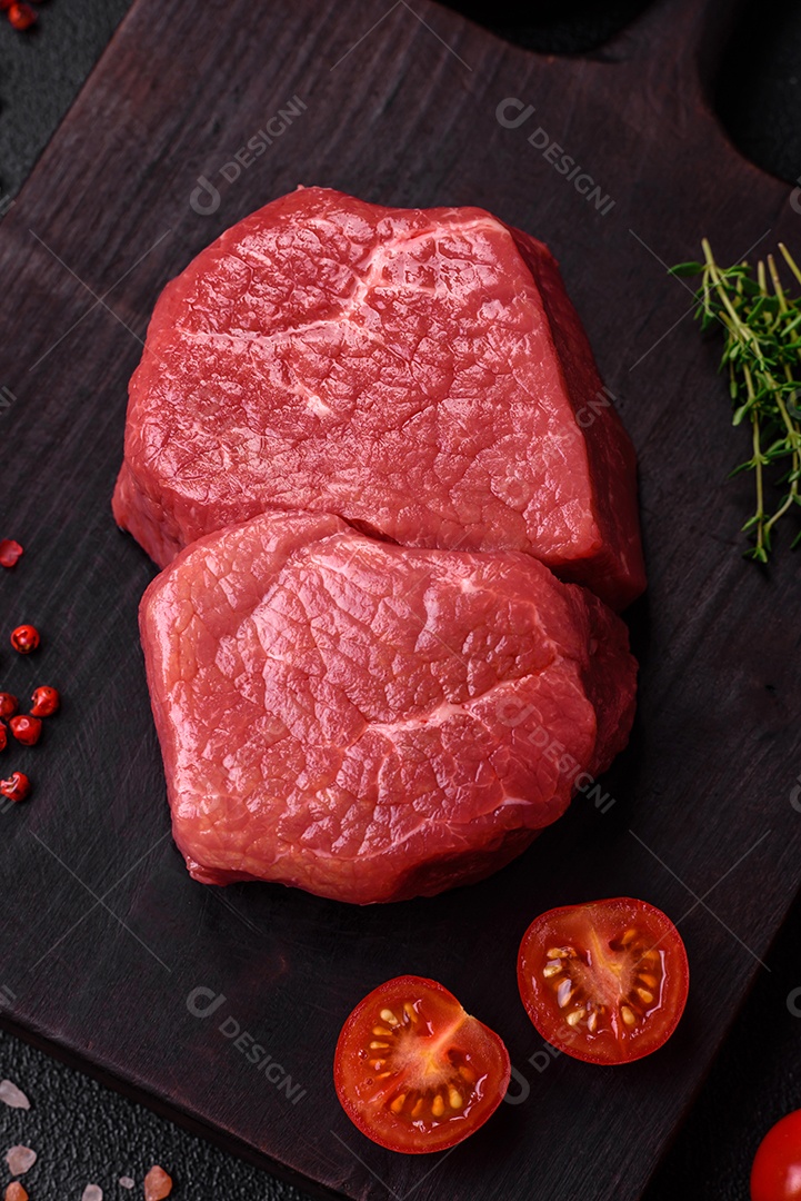 Bife de filé mignon cru com sal, especiarias e ervas em um fundo escuro de concreto