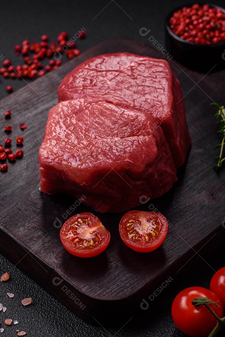 Bife de filé mignon cru com sal, especiarias e ervas em um fundo escuro de concreto