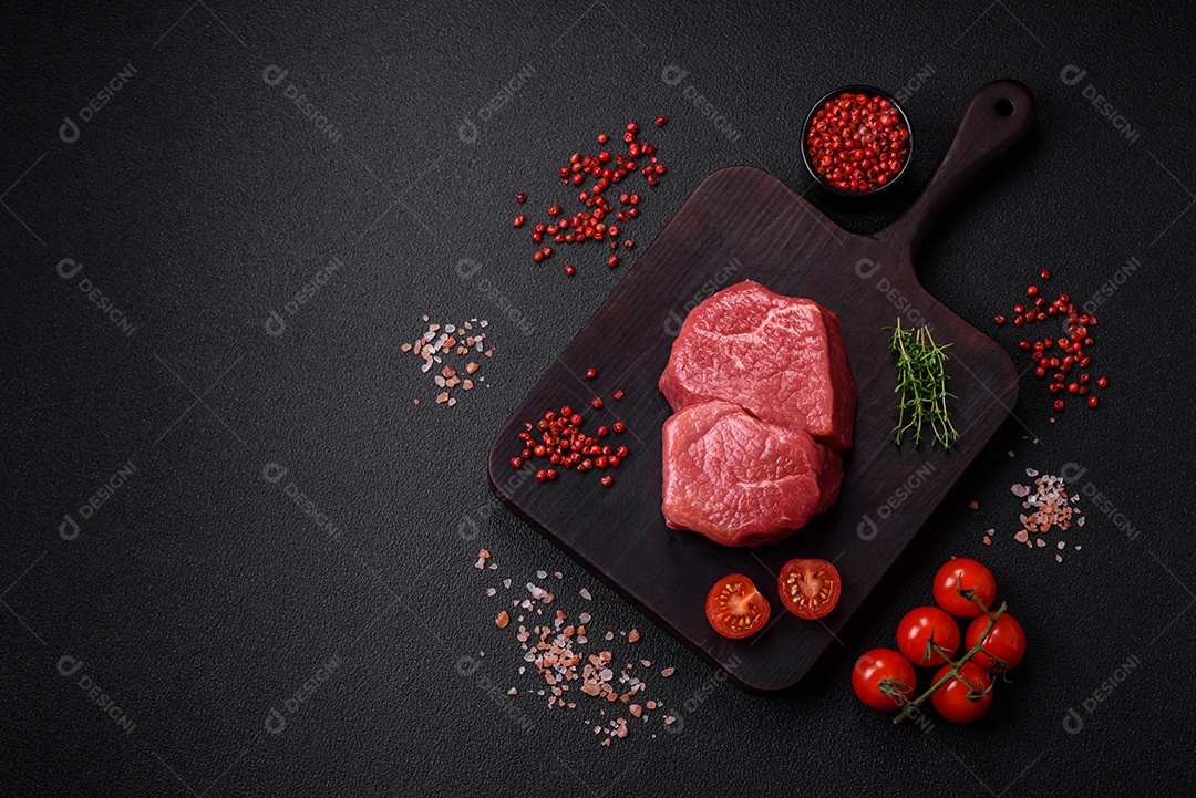 Bife de filé mignon cru com sal, especiarias e ervas em um fundo escuro de concreto