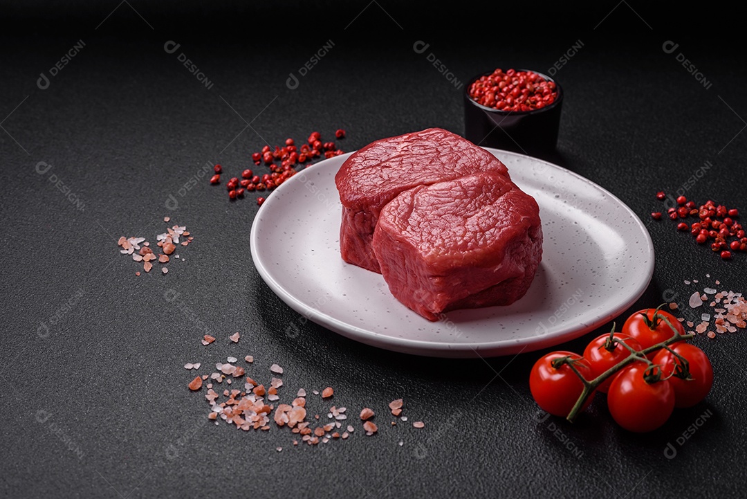 Bife de filé mignon cru com sal, especiarias e ervas em um fundo escuro de concreto