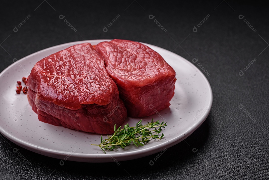 Bife de filé mignon cru com sal, especiarias e ervas em um fundo escuro de concreto
