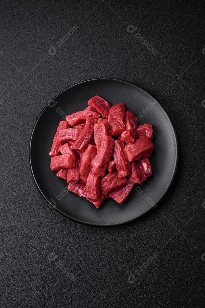 Carne orgânica crua ou cordeiro cortado em fatias com sal, especiarias e ervas sobre um fundo escuro de concreto