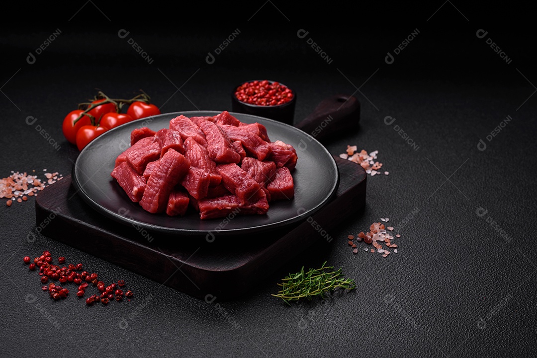 Carne orgânica crua ou cordeiro cortado em fatias com sal, especiarias e ervas sobre um fundo escuro de concreto