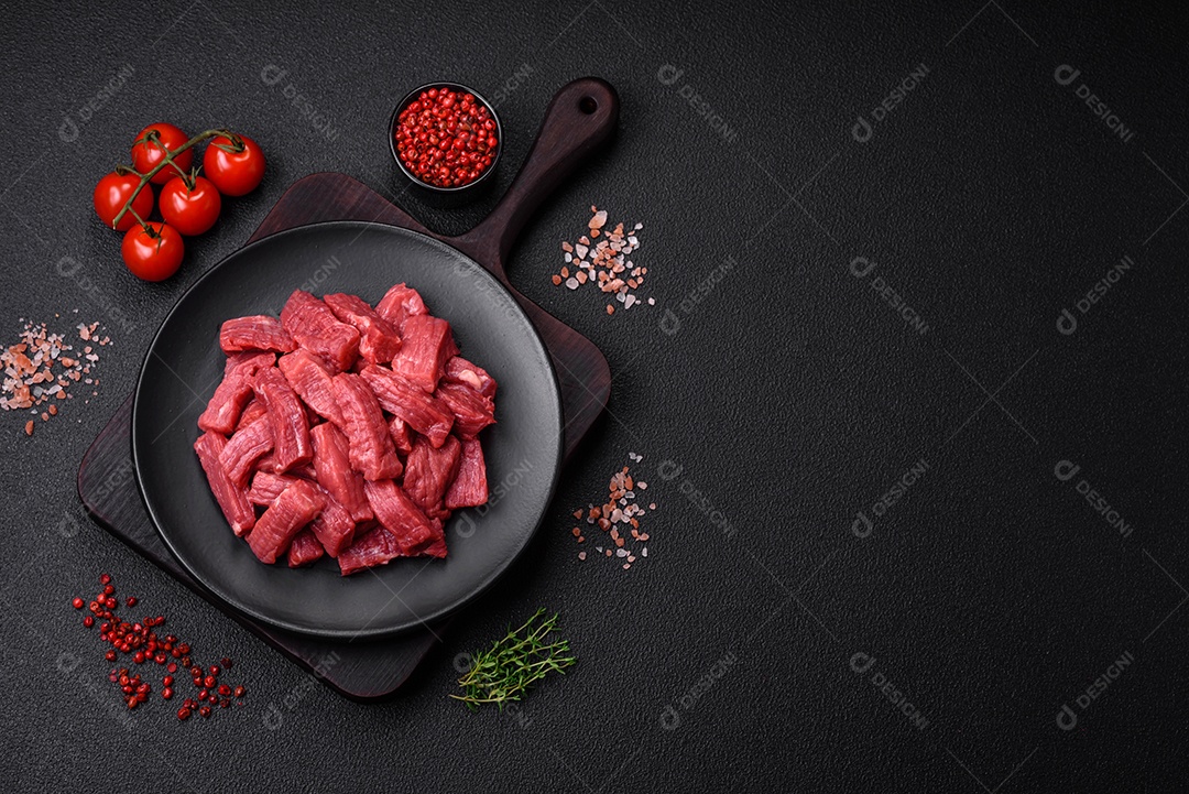 Carne orgânica crua ou cordeiro cortado em fatias com sal, especiarias e ervas sobre um fundo escuro de concreto