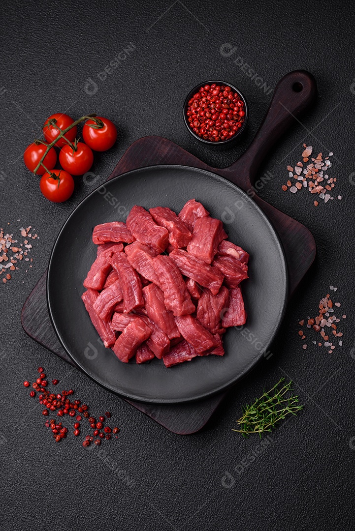 Carne orgânica crua ou cordeiro cortado em fatias com sal, especiarias e ervas sobre um fundo escuro de concreto