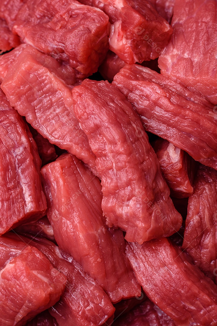 Carne orgânica crua ou cordeiro cortado em fatias com sal, especiarias e ervas sobre um fundo escuro de concreto