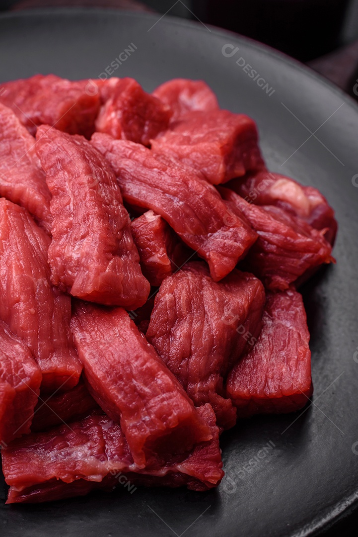 Carne orgânica crua ou cordeiro cortado em fatias com sal, especiarias e ervas sobre um fundo escuro de concreto