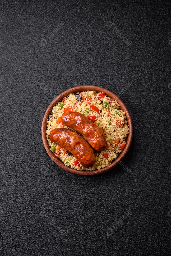 Deliciosas salsichas de frango ou porco assadas na grelha e cuscuz com legumes sobre um fundo escuro de concreto