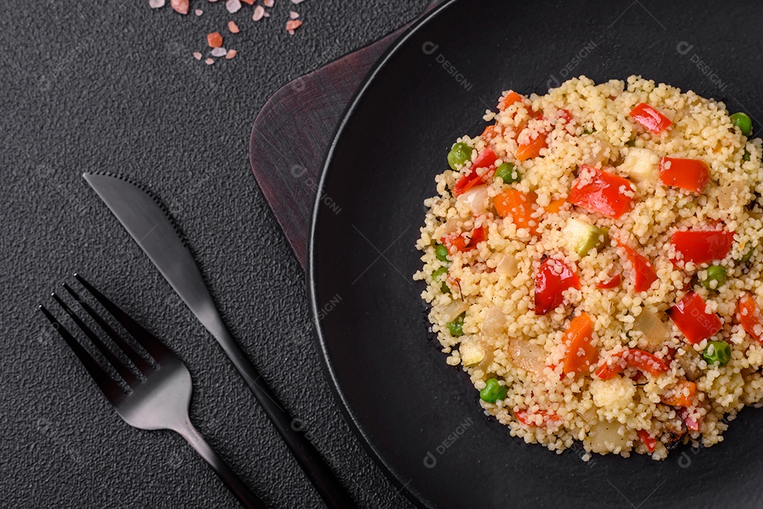 Delicioso cuscuz com cubos de legumes grelhados com sal e especiarias sobre um fundo escuro de concreto