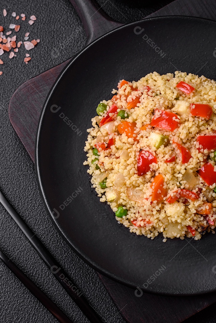 Delicioso cuscuz com cubos de legumes grelhados com sal e especiarias sobre um fundo escuro de concreto