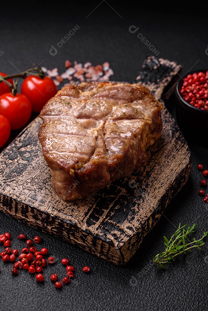 Delicioso suculento bife de porco ou de vaca cozido na grelha com sal e especiarias sobre um fundo de concreto texturizado