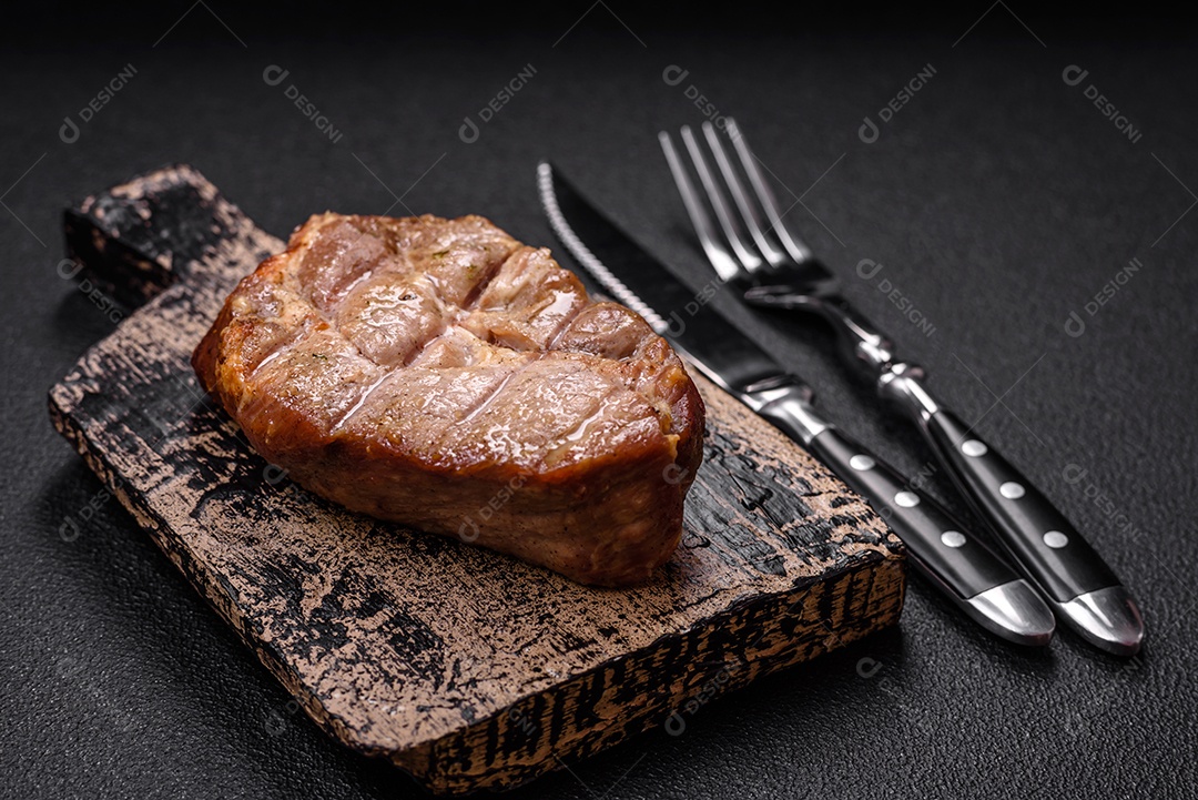 Delicioso suculento bife de porco ou de vaca cozido na grelha com sal e especiarias sobre um fundo de concreto texturizado