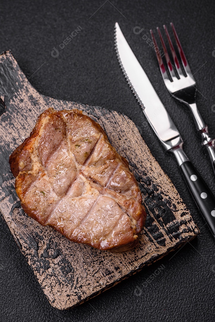 Delicioso suculento bife de porco ou de vaca cozido na grelha com sal e especiarias sobre um fundo de concreto texturizado