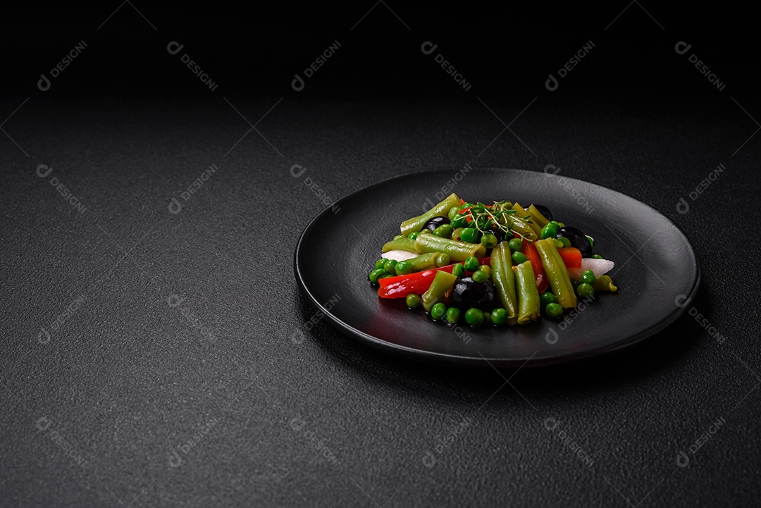Deliciosa salada fresca de feijão verde, ervilha, pimentão e queijo com sal e especiarias sobre um fundo escuro de concreto