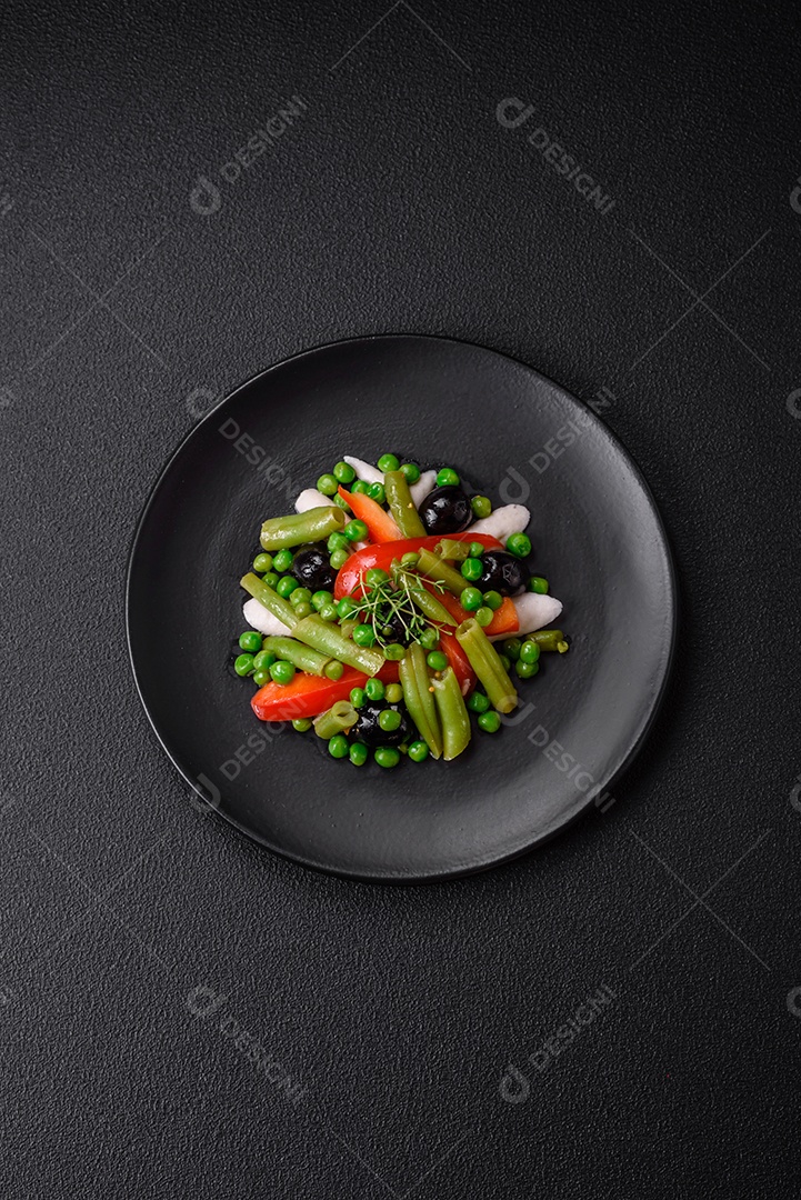 Deliciosa salada fresca de feijão verde, ervilha, pimentão e queijo com sal e especiarias sobre um fundo escuro de concreto