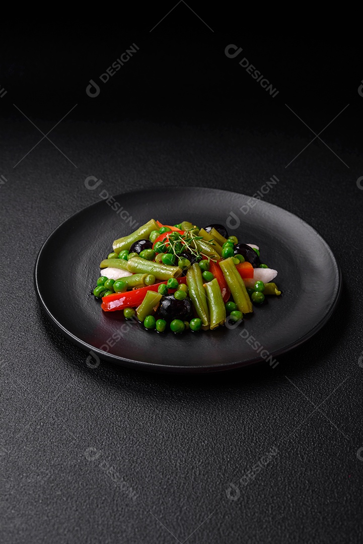 Deliciosa salada fresca de feijão verde, ervilha, pimentão e queijo com sal e especiarias sobre um fundo escuro de concreto