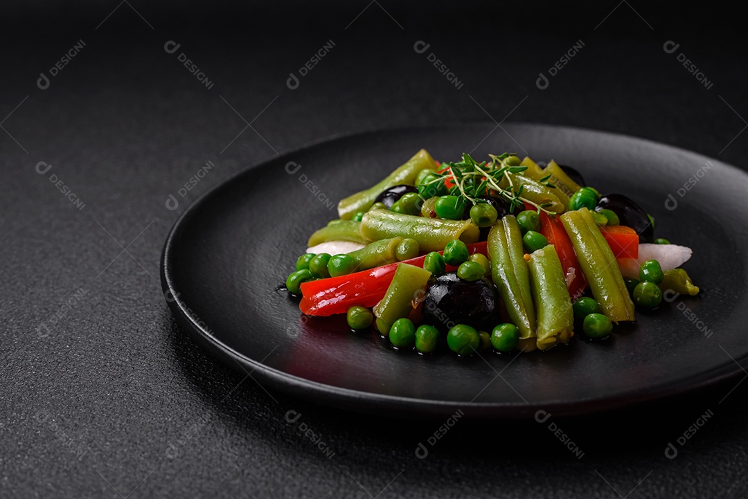 Deliciosa salada fresca de feijão verde, ervilha, pimentão e queijo com sal e especiarias sobre um fundo escuro de concreto