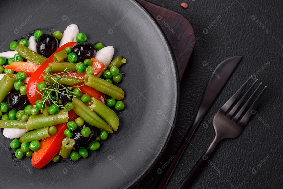 Deliciosa salada fresca de feijão verde, ervilha, pimentão e queijo com sal e especiarias sobre um fundo escuro de concreto