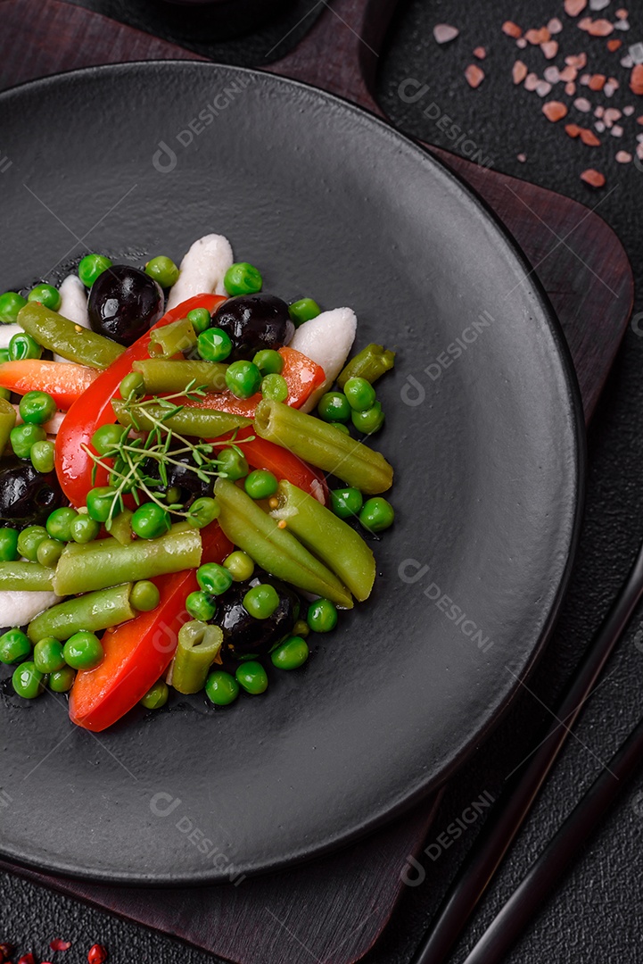 Deliciosa salada fresca de feijão verde, ervilha, pimentão e queijo com sal e especiarias sobre um fundo escuro de concreto