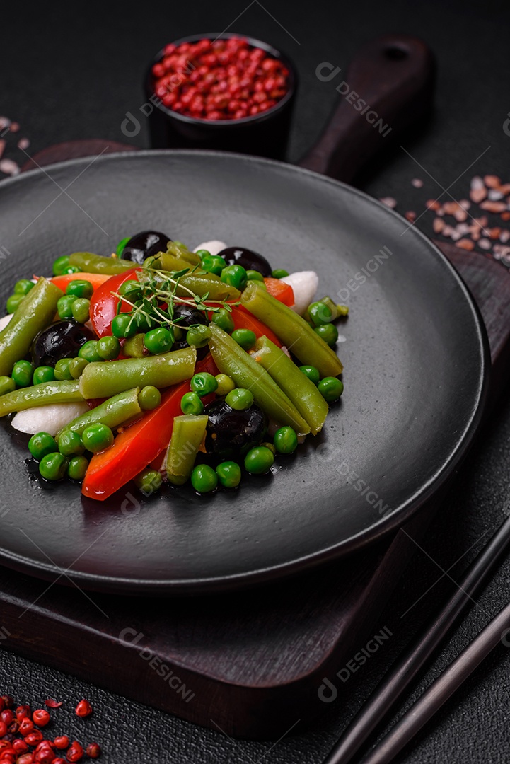 Deliciosa salada fresca de feijão verde, ervilha, pimentão e queijo com sal e especiarias sobre um fundo escuro de concreto